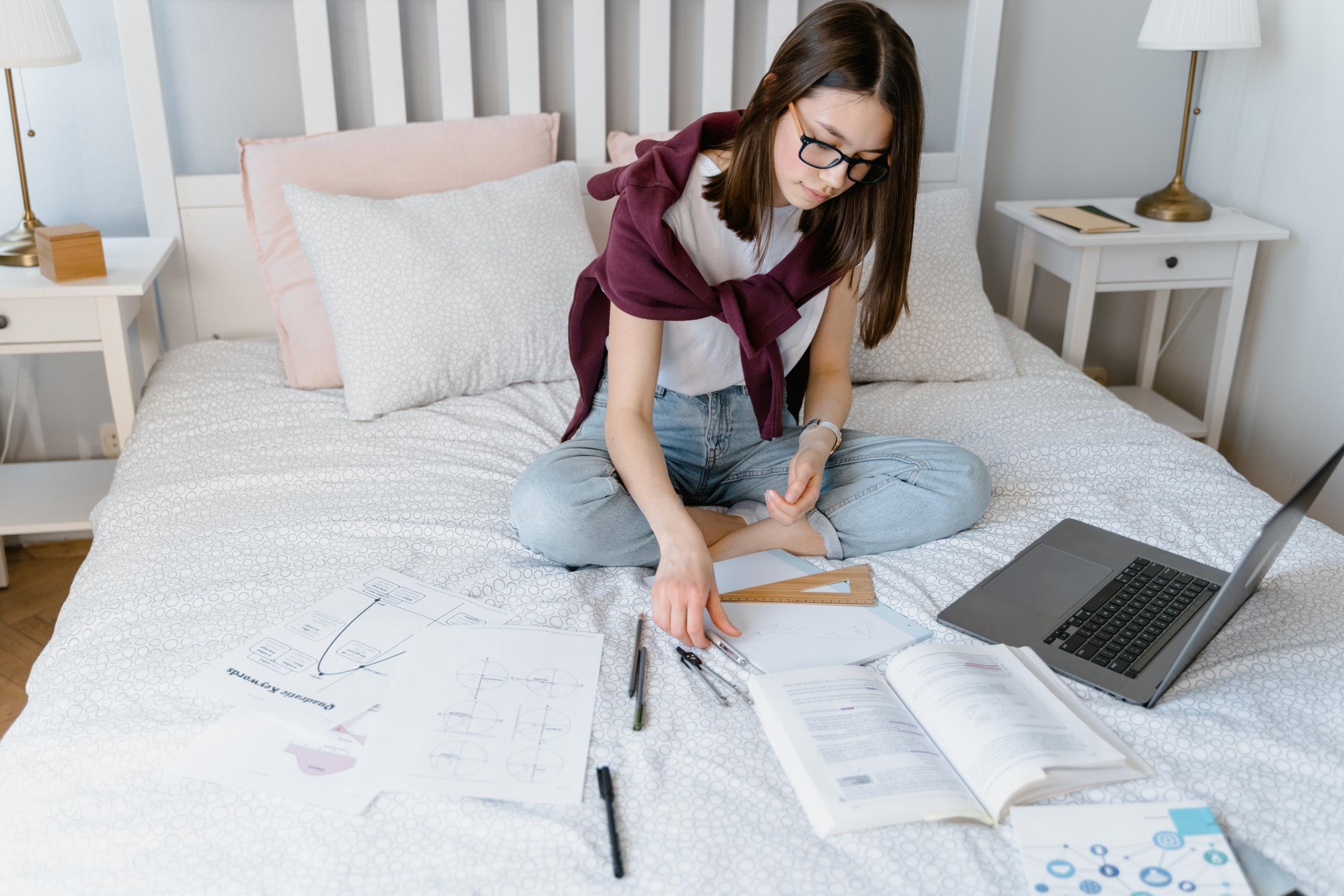 aluna a estudar na cama com livros e computador