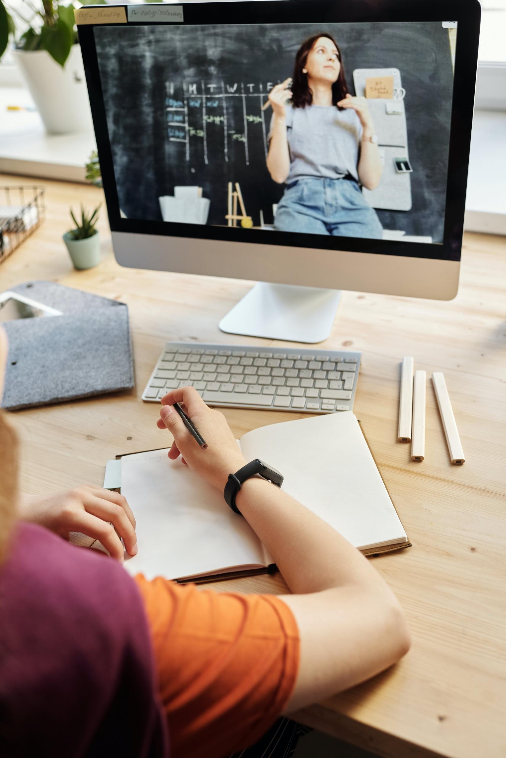 jovem a tirar notas em frente a computador