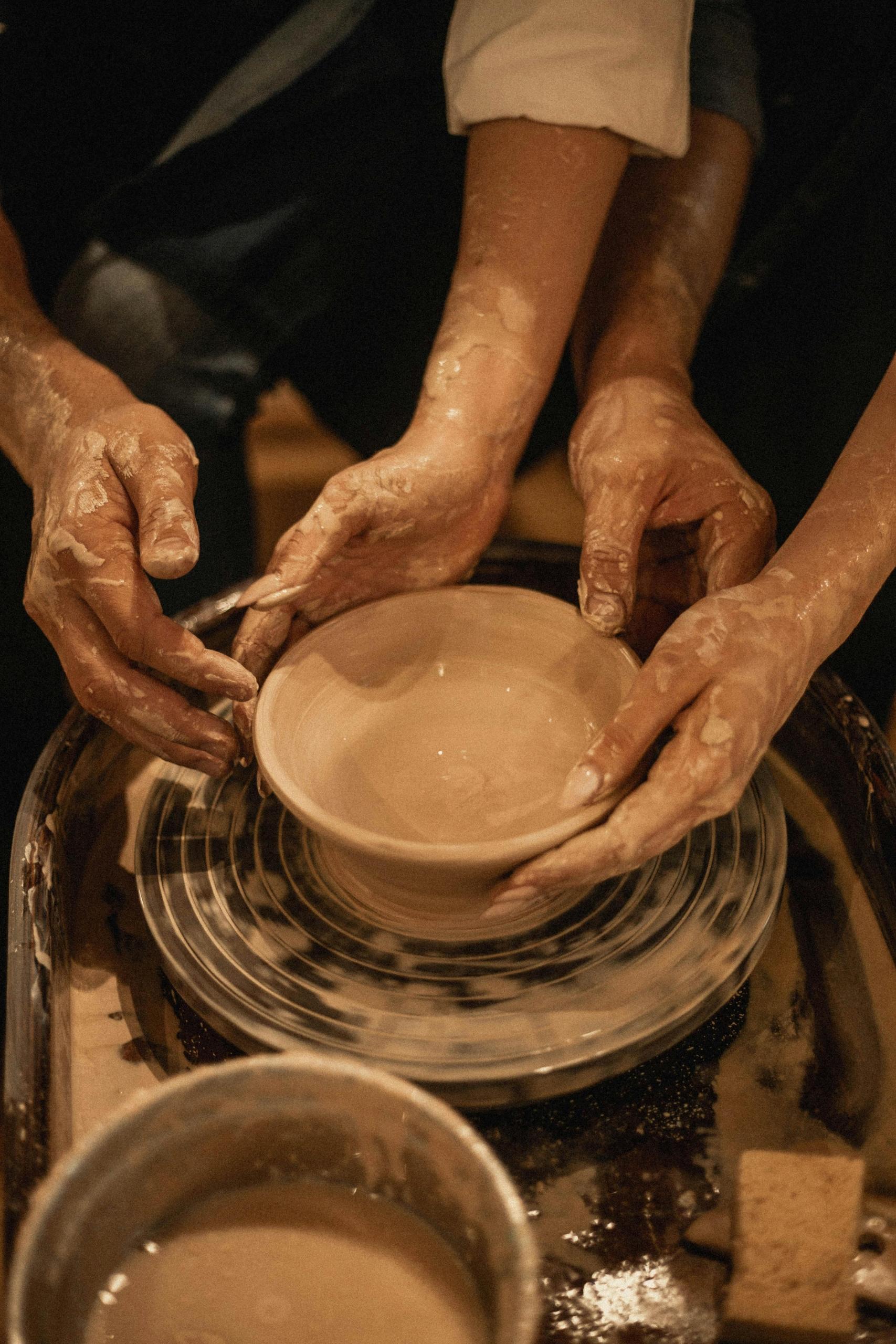 dois pares de mãos a trabalhar numa taça de barro