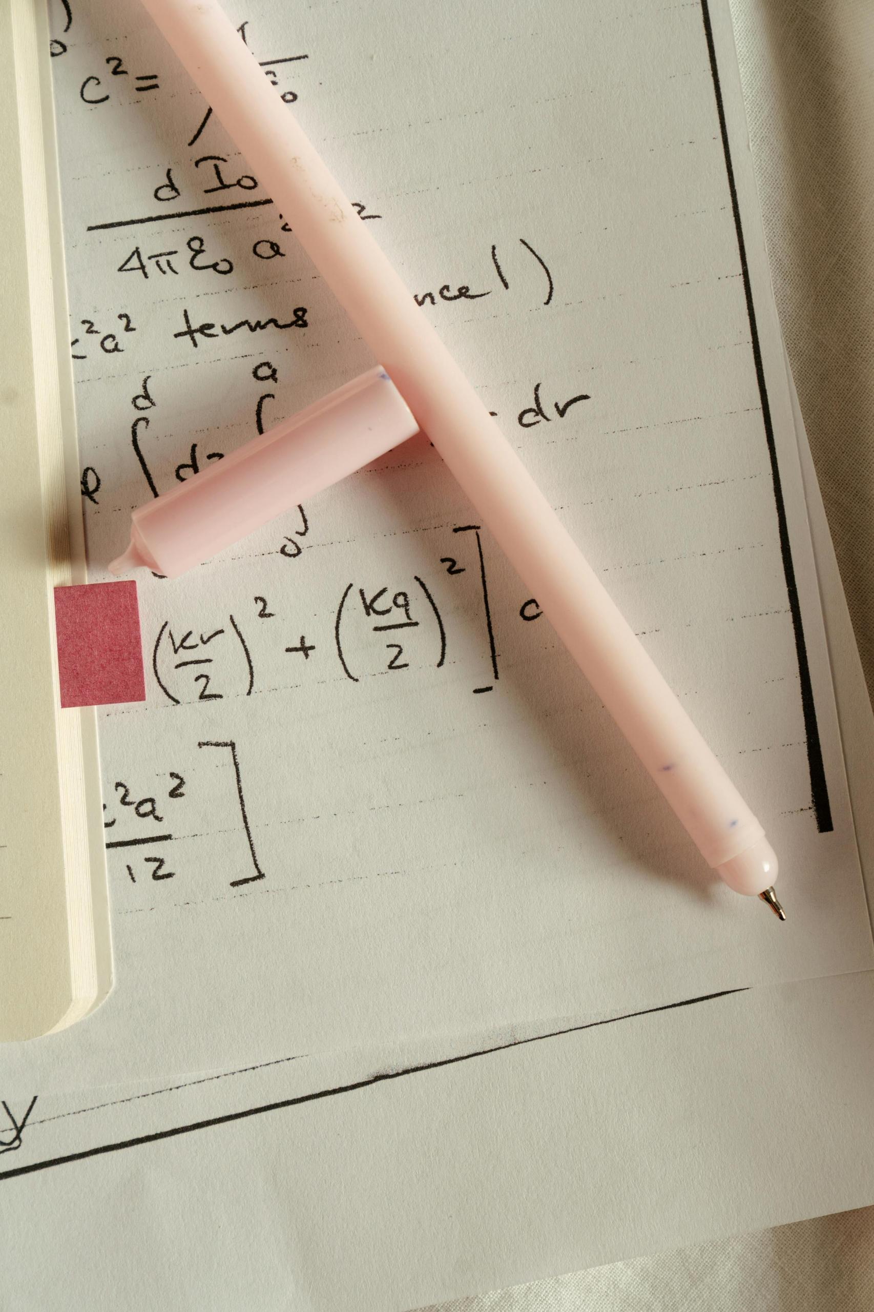 folha com cálculos matemáticos e caneta rosa
