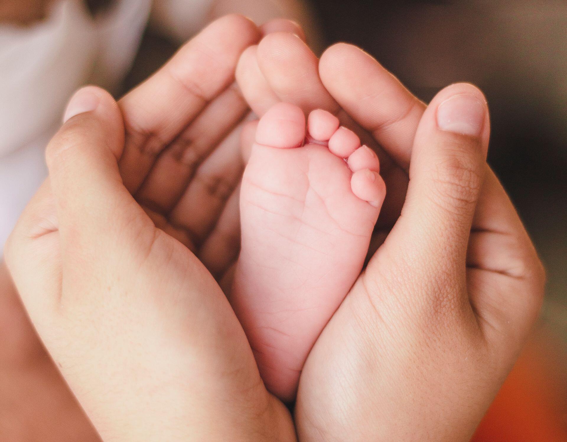 mãos de adulto à volta de pé de bebé