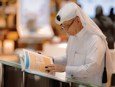 رجل يرتدي الثوب والغترة يتصفح بتركيز كتابا مصورا في معرض الكتاب.