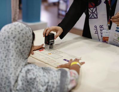 طفلة صغيرة تشارك في نشاط تفاعلي  وتختم ورقة بمساعدة أحد المتطوعين في المعرض.
