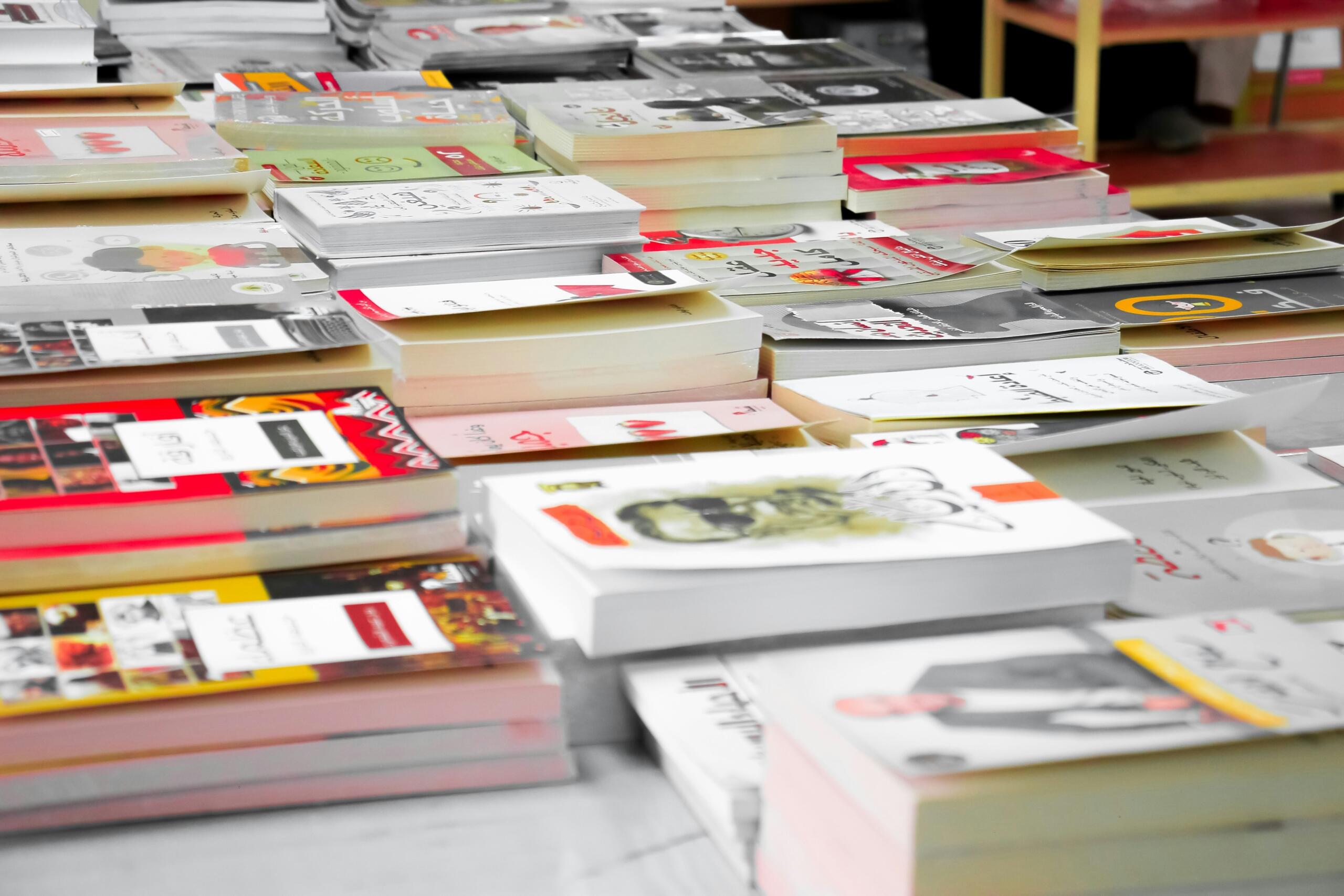 مجموعة متنوعة من الكتب مرتبة أفقيا فوق بعضها البعض في معرض أو مكتبة.