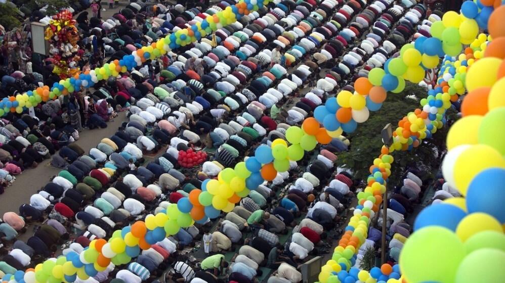 مصلون يؤدون صلاة العيد في ساحة خارجية مفتوحة، وسط أجواء روحانية وفرِحة مع تجمعات كبيرة من العائلات والمجتمع.