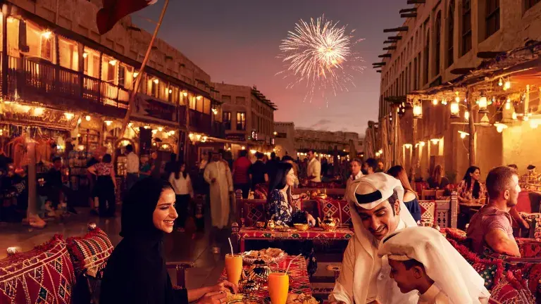 عائلة تحتفل بعيد الأضحى في قطر في أجواء خارجية مبهجة، يرتدون الملابس التقليدية ويتبادلون التهاني وسط زينة العيد وأجواء احتفالية دافئة.