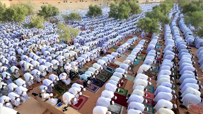 مصلون يؤدون صلاة العيد في ساحة خارجية مفتوحة، وسط أجواء روحانية وفرِحة مع تجمعات كبيرة من العائلات والمجتمع.