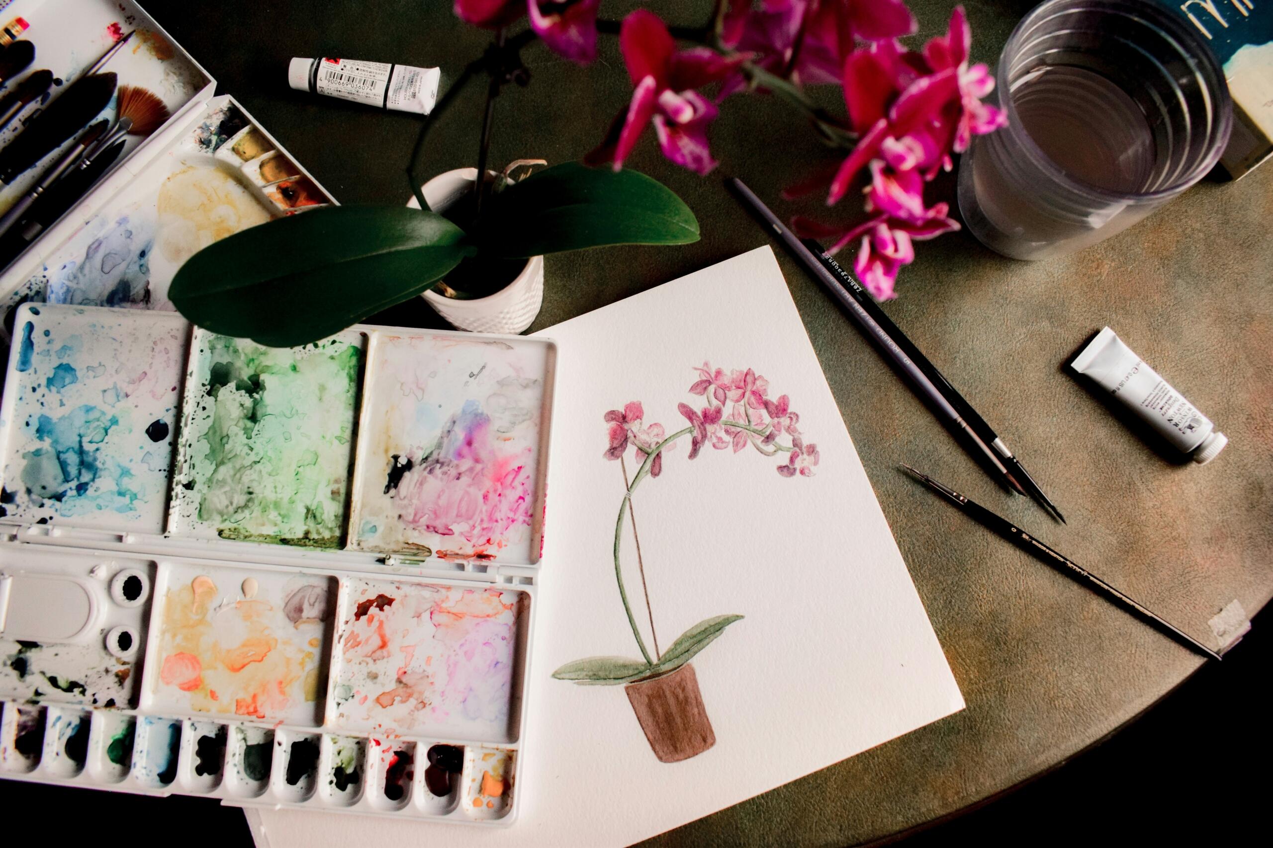 صورة لطاولة فوقها لوحة مائية وتحيط بالرسمة أدوات ومستلزمات الرسم.