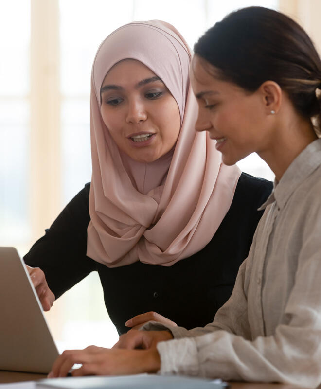معلمة تجلس بجوار طالبة، أمامهما جهاز حاسوب في جلسة تدريس خاصة.
