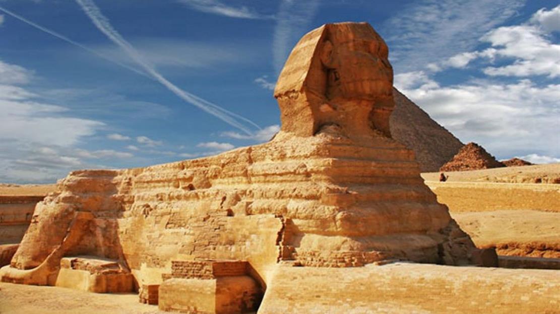 الأهرامات وأبو الهول في هضبة الجيزة، مصر، حيث تظهر الأهرامات الحجرية الضخمة في الخلفية وسط الصحراء.