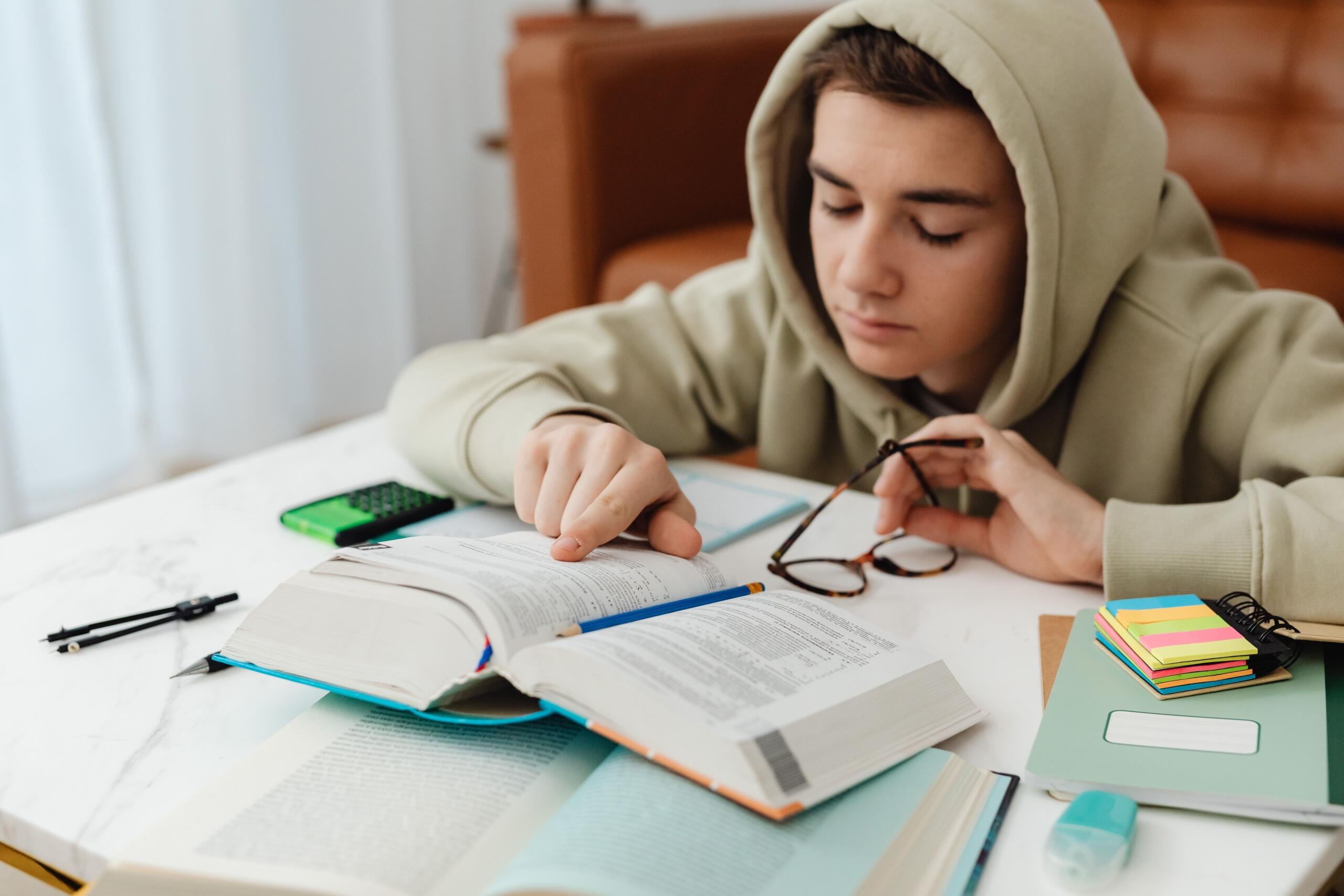 طالب يقرأ كتابًا ويراجع دروسه بهدوء وتركيز في بيئة مناسبة للدراسة