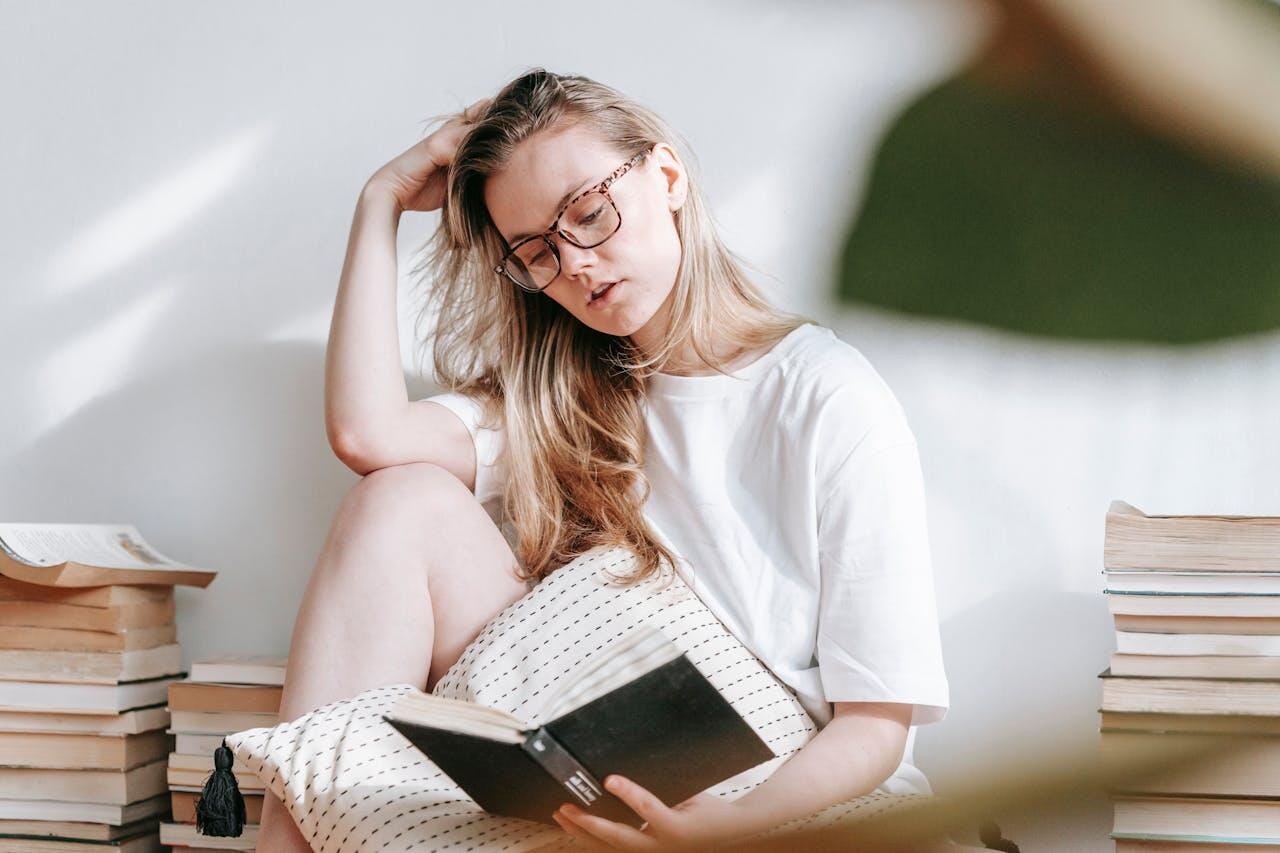 jeune femme a lunette contre le mur assise lisant un livre