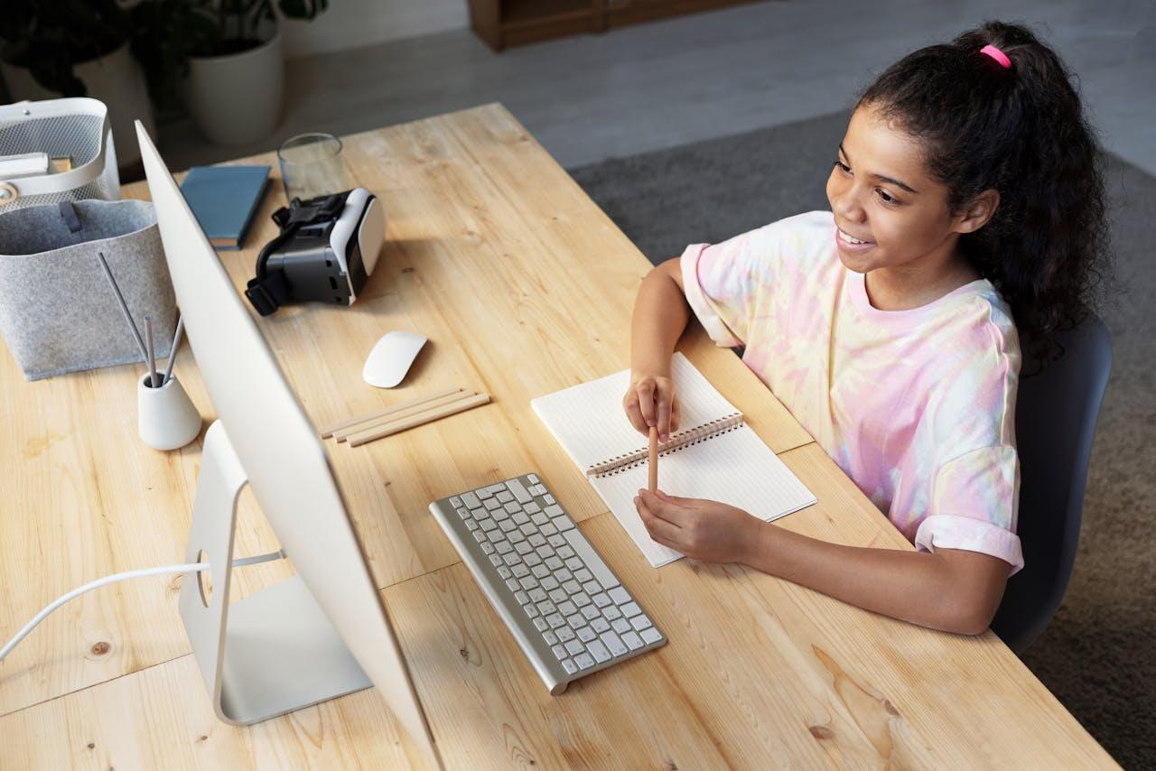 jeune fille souriant sur son bureau devant son ecran d ordinateur avec un crayon et un cahier