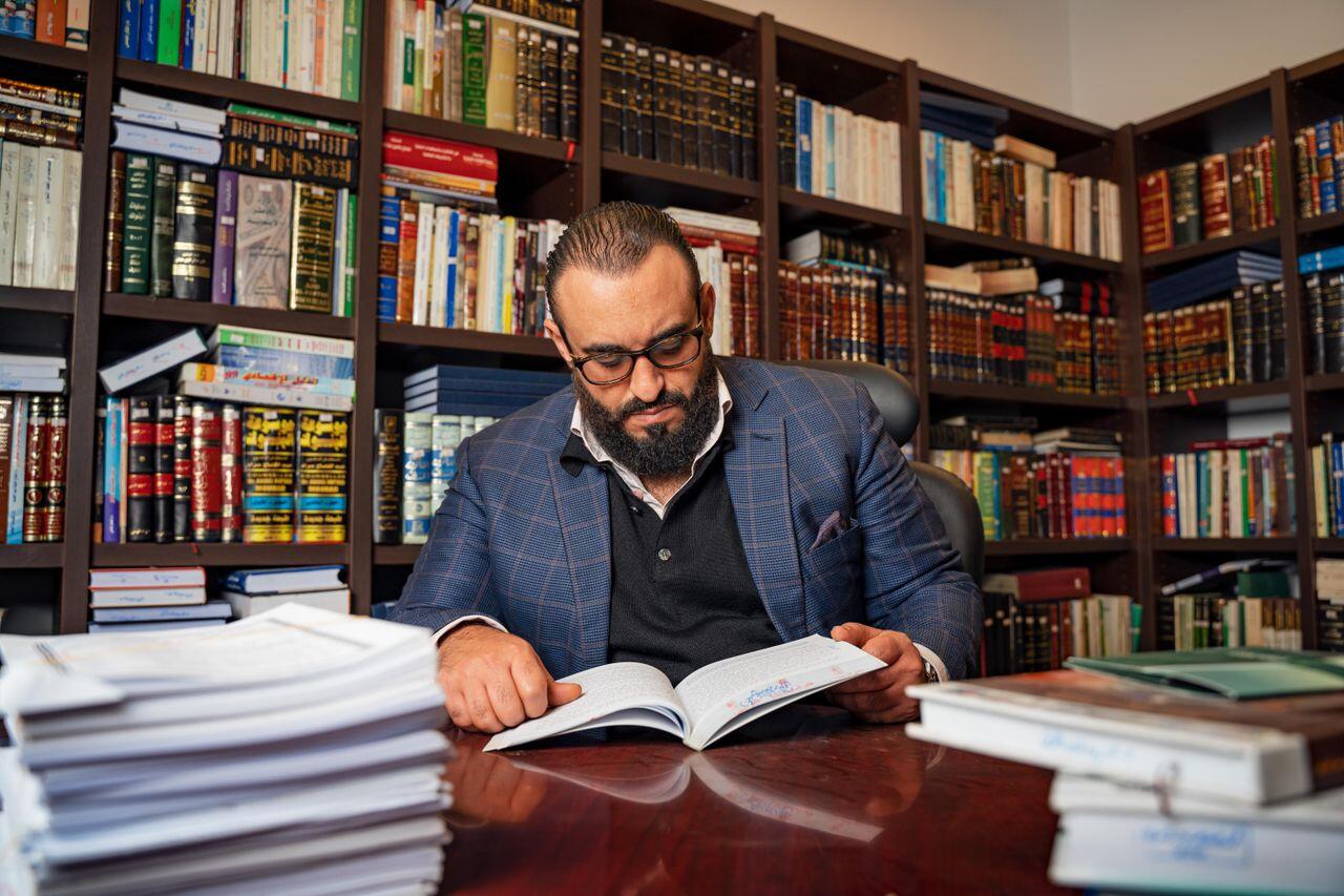 homme avec un bouquin sur un bureau devant des etageres de livres