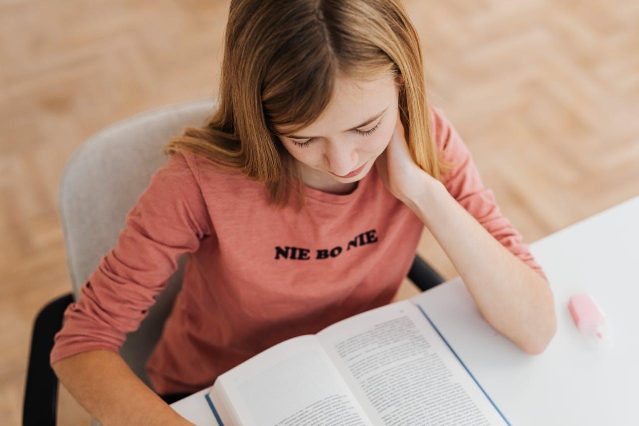 fille avec un tee-shirt a manches longues revisant a son bureau en lisant un livre avec un surligneur rose