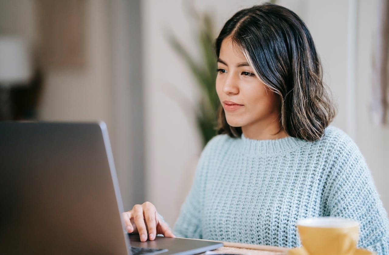 fille en pull bleu devant son ordi avec une tasse