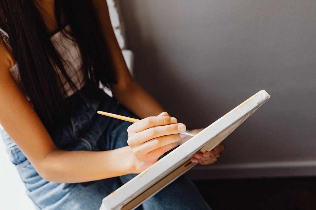 jeune fille aux cheveux long et en salopette au sol avec un crayon et un cahier
