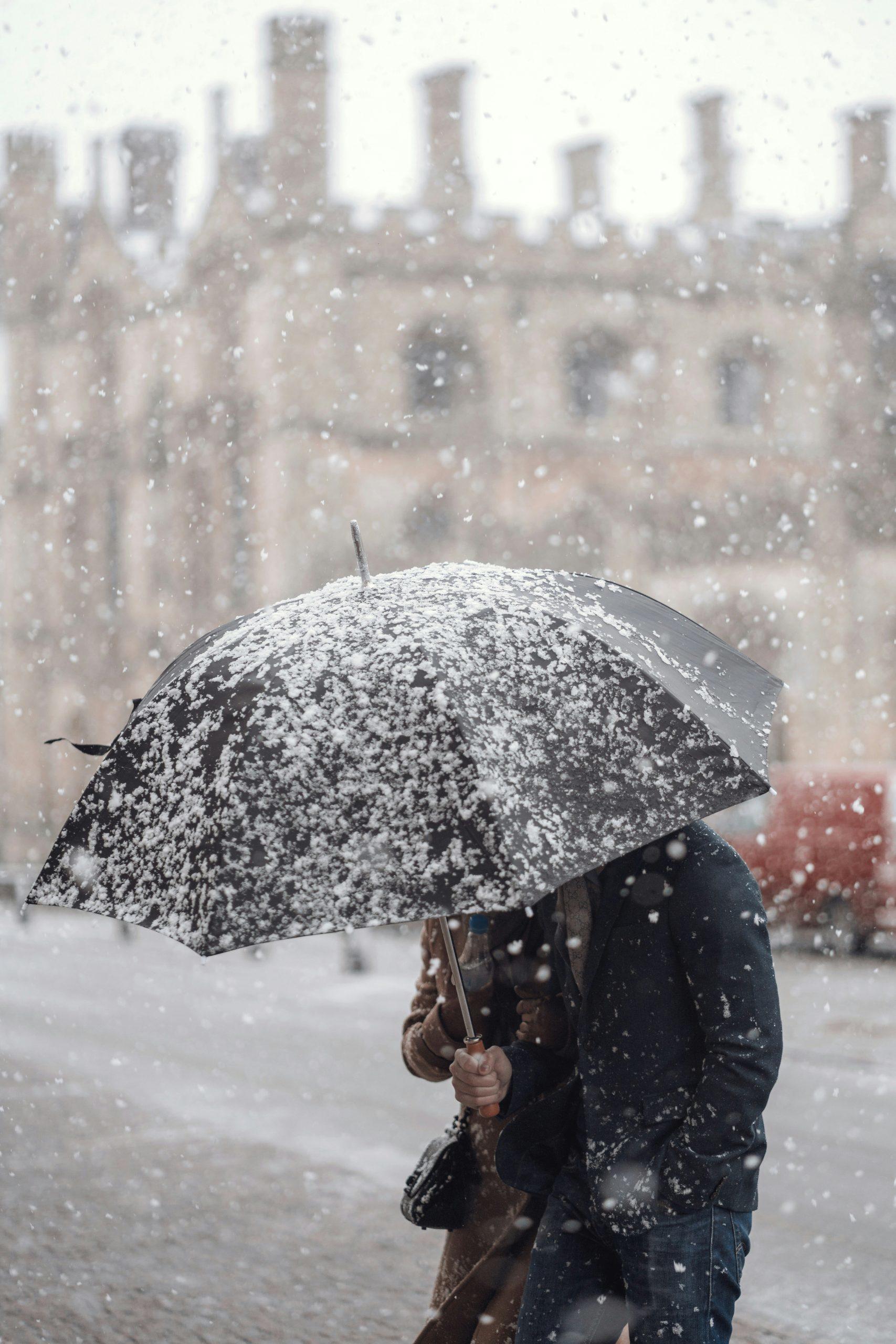 Un homme s'abrite de la neige avec un parapluie.