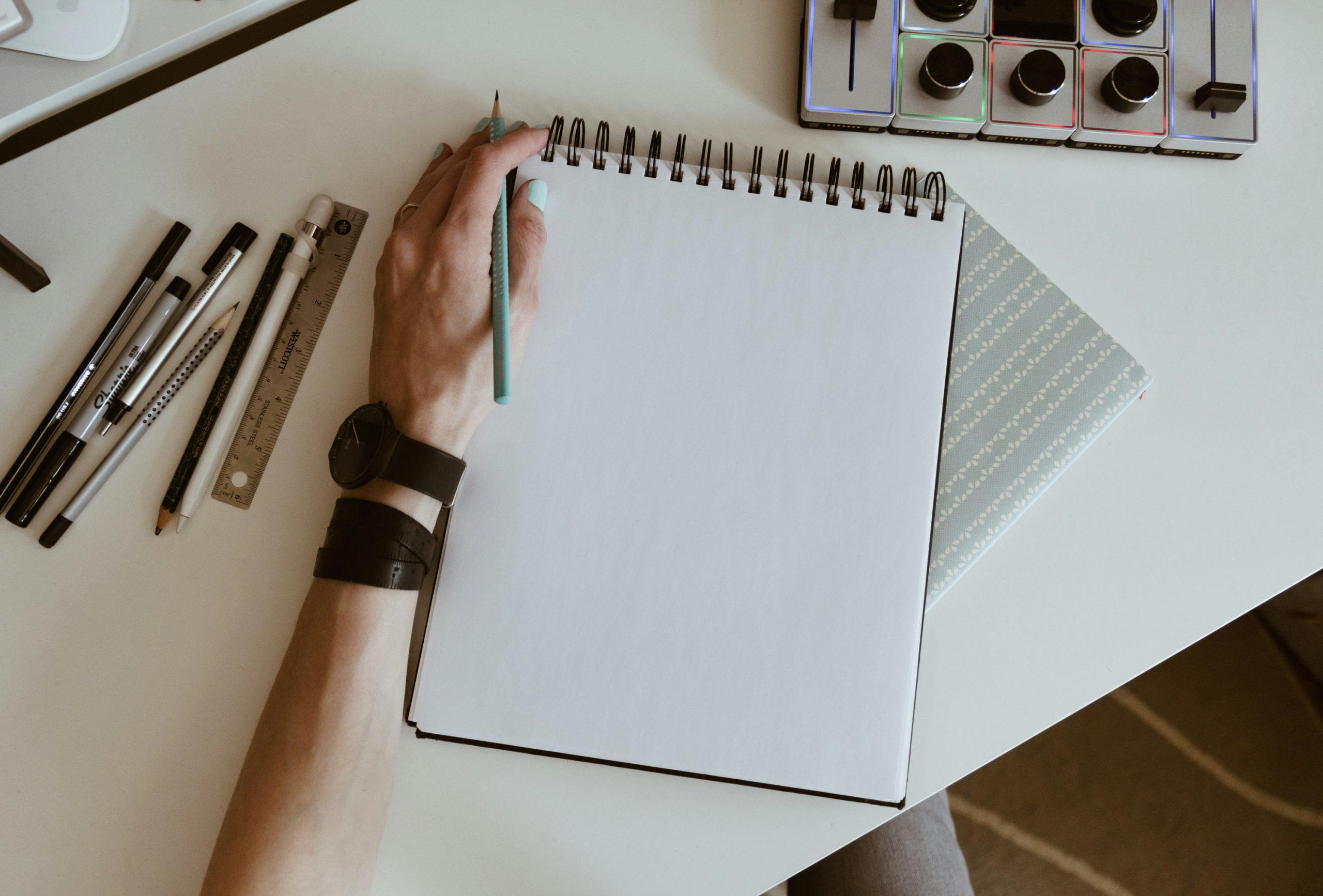 Un cahier blanc devant une main et un stylo.