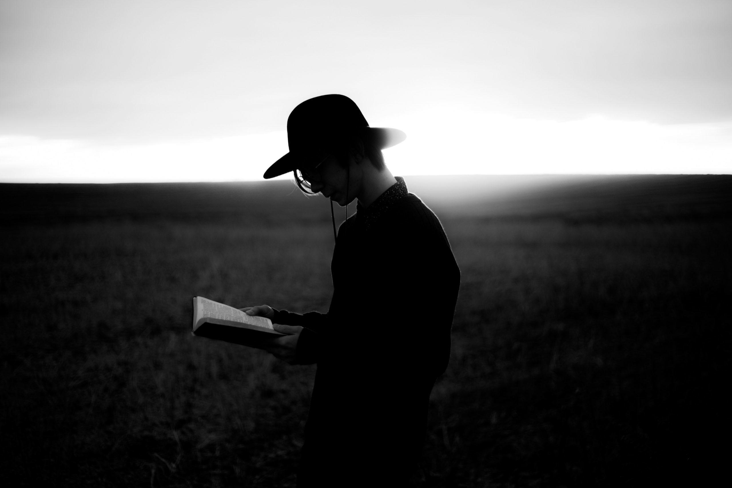 Un homme avec un chapeau lit un livre dans un champ.