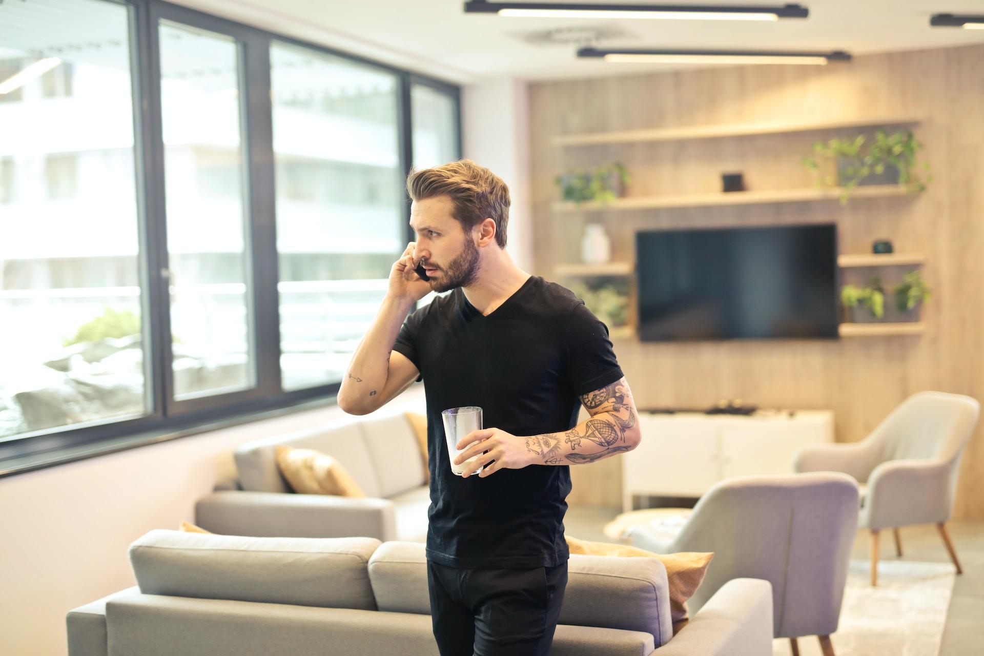 homme en tee-shirt noir au téléphone dans un salon