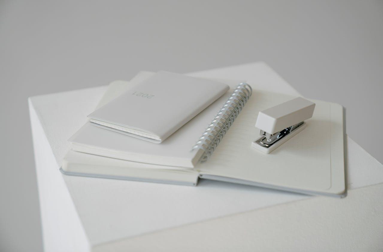 cahier blanc et agrapheuse blanche sur table blanche