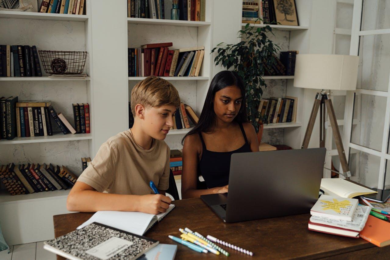 deux adolescents etudiant sur un bureau avec un laptop et des cahiers