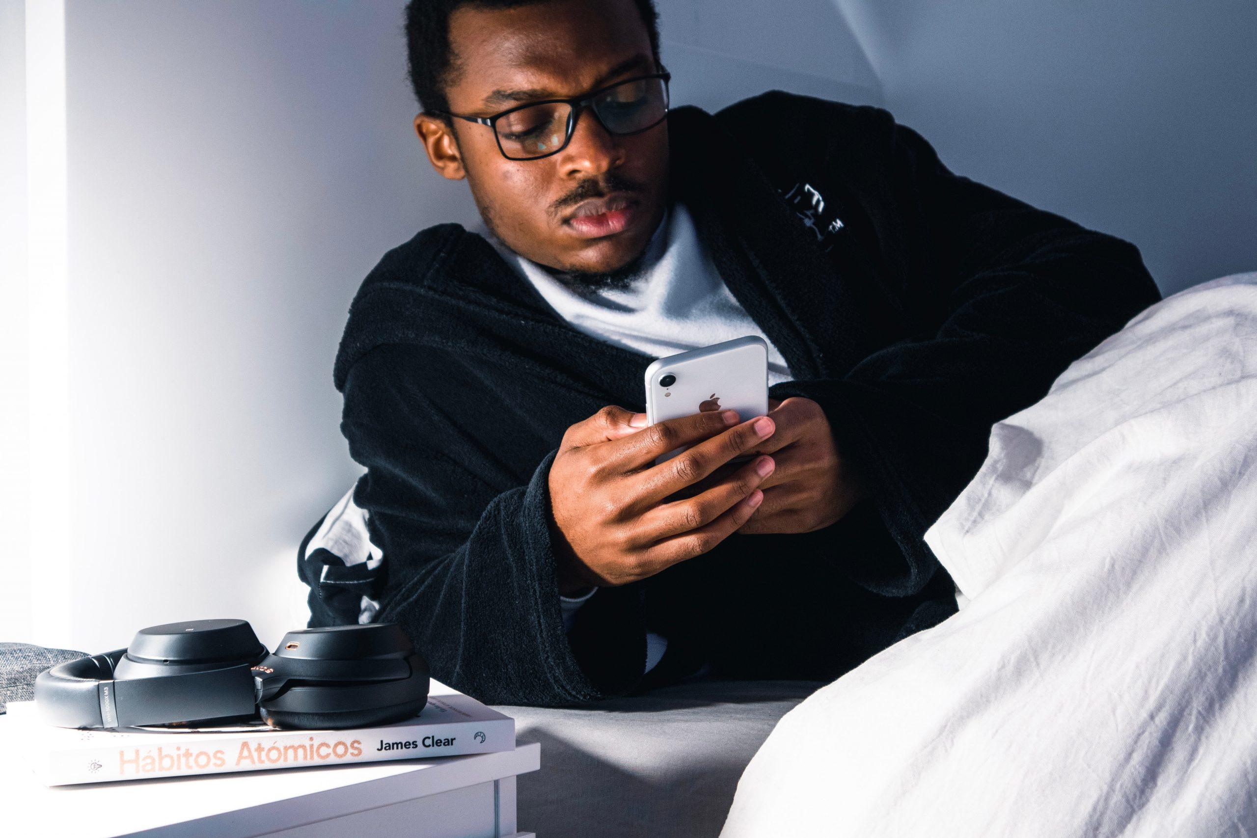 Un jeune homme regarde son téléphone dans son lit.