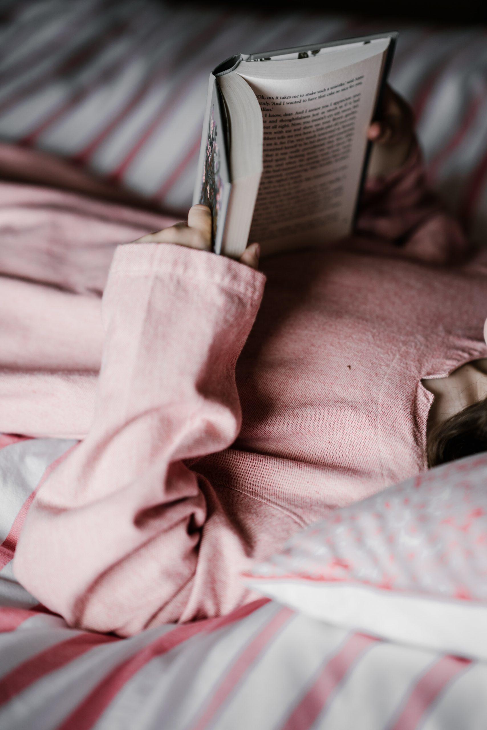 Une jeune femme lit un livre en anglais sur son lit.