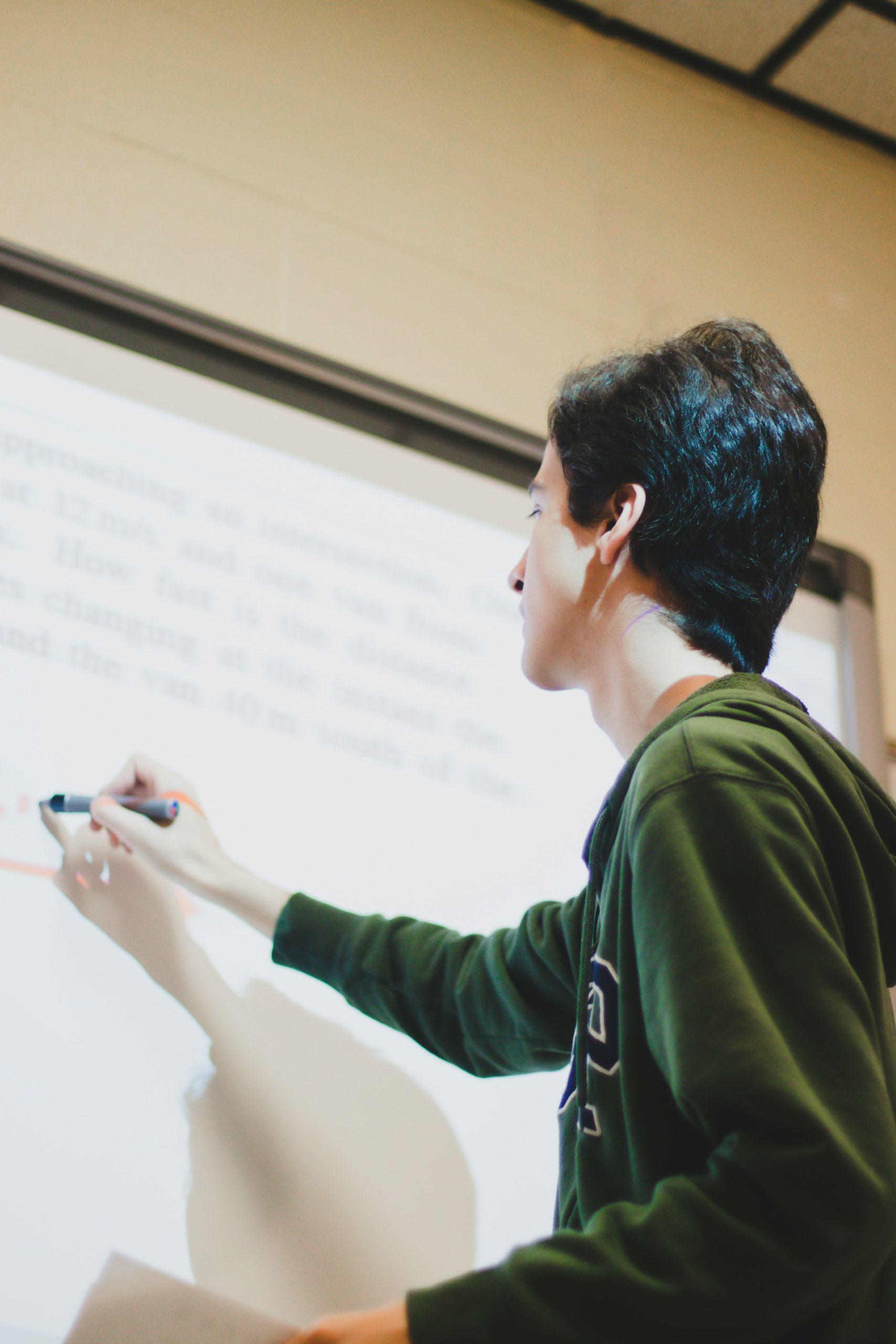 Un élève écrit des formules sur un tableau blanc.