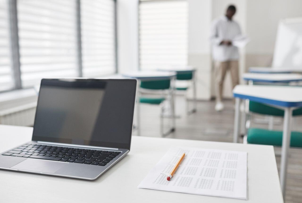 salle de classe avec un prof au bout et le laptop devant sur le bureau