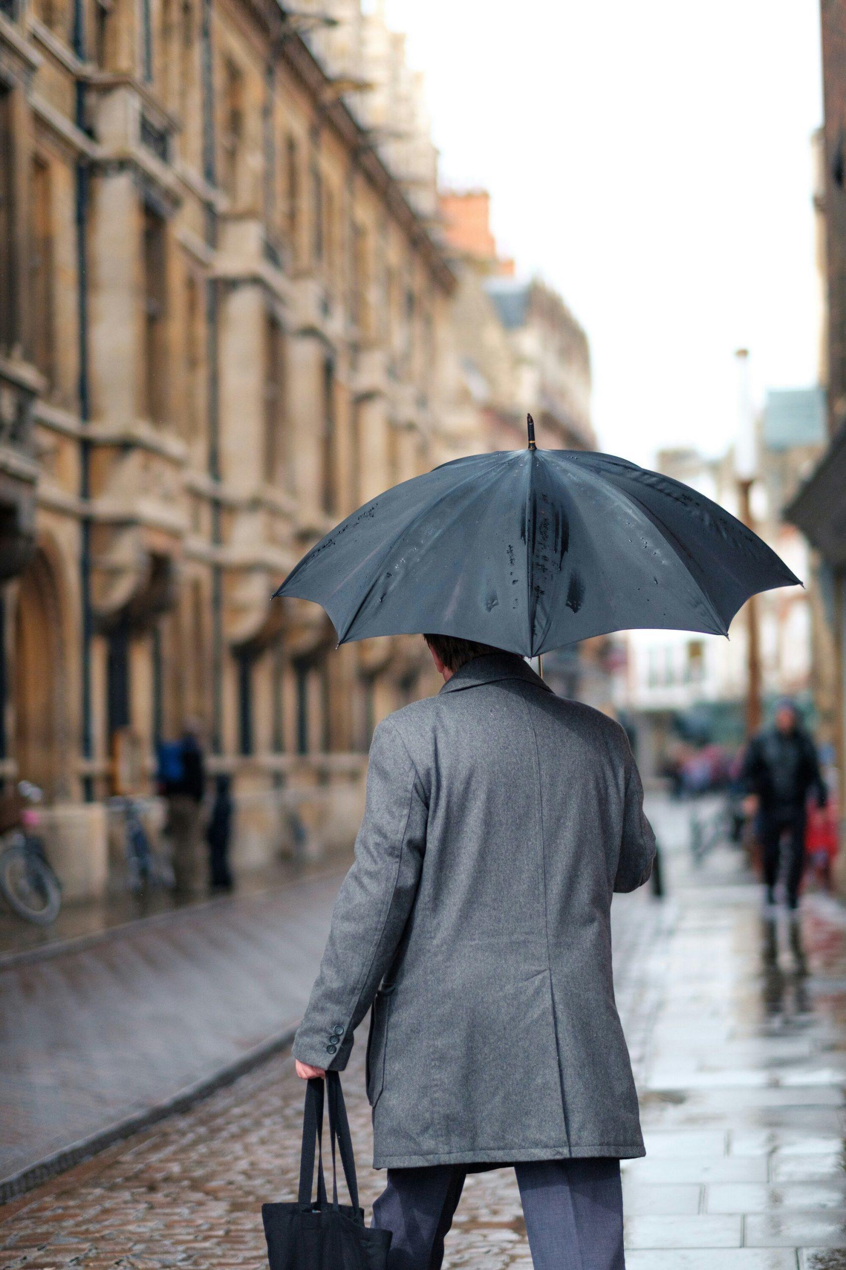 Un homme avec un parapluie marche de dos dans une rue anglaise.