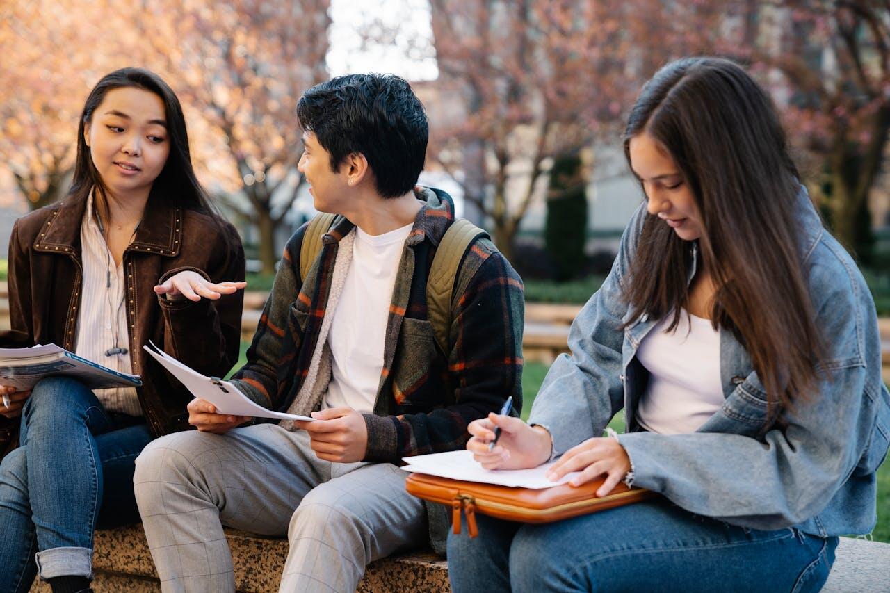 trois jeunes dehors assis portant leurs sac a dos en train d etudier avec leurs feuilles