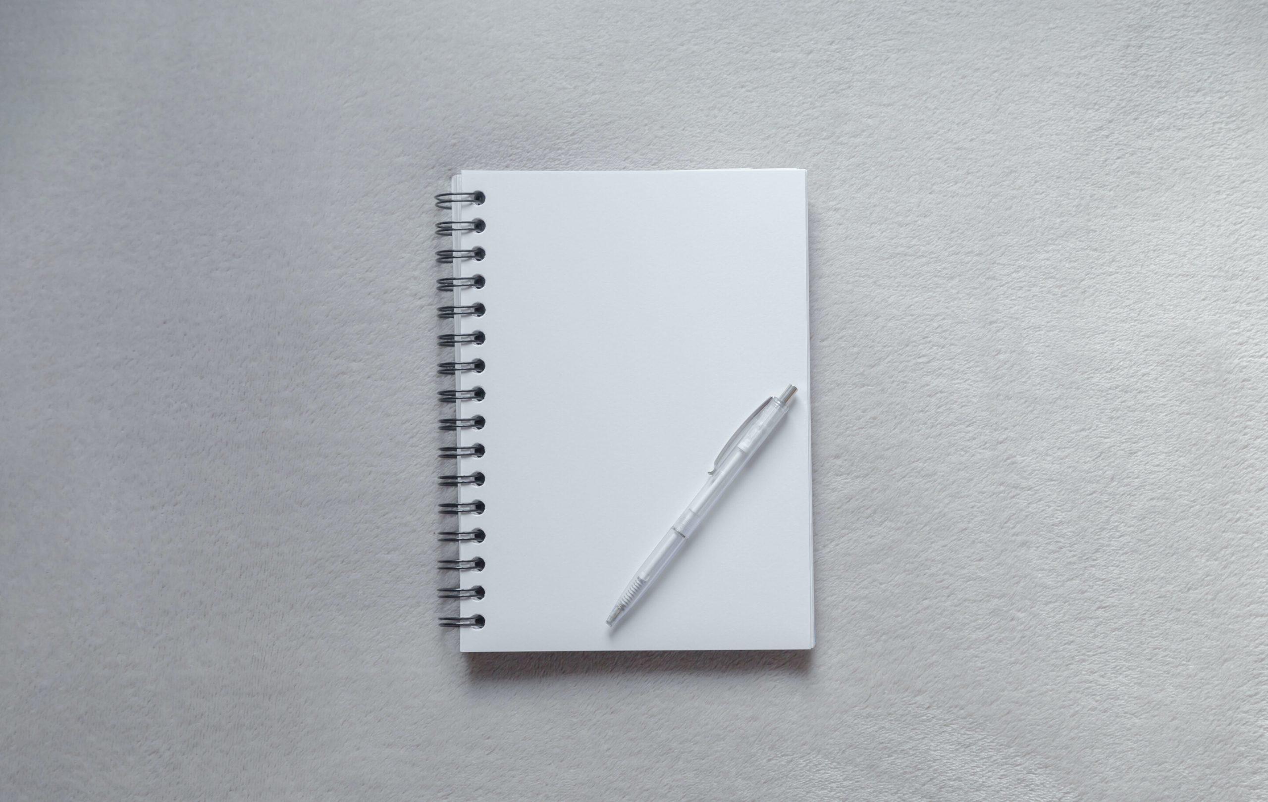 Un carnet blanc posé sur avec un stylo.