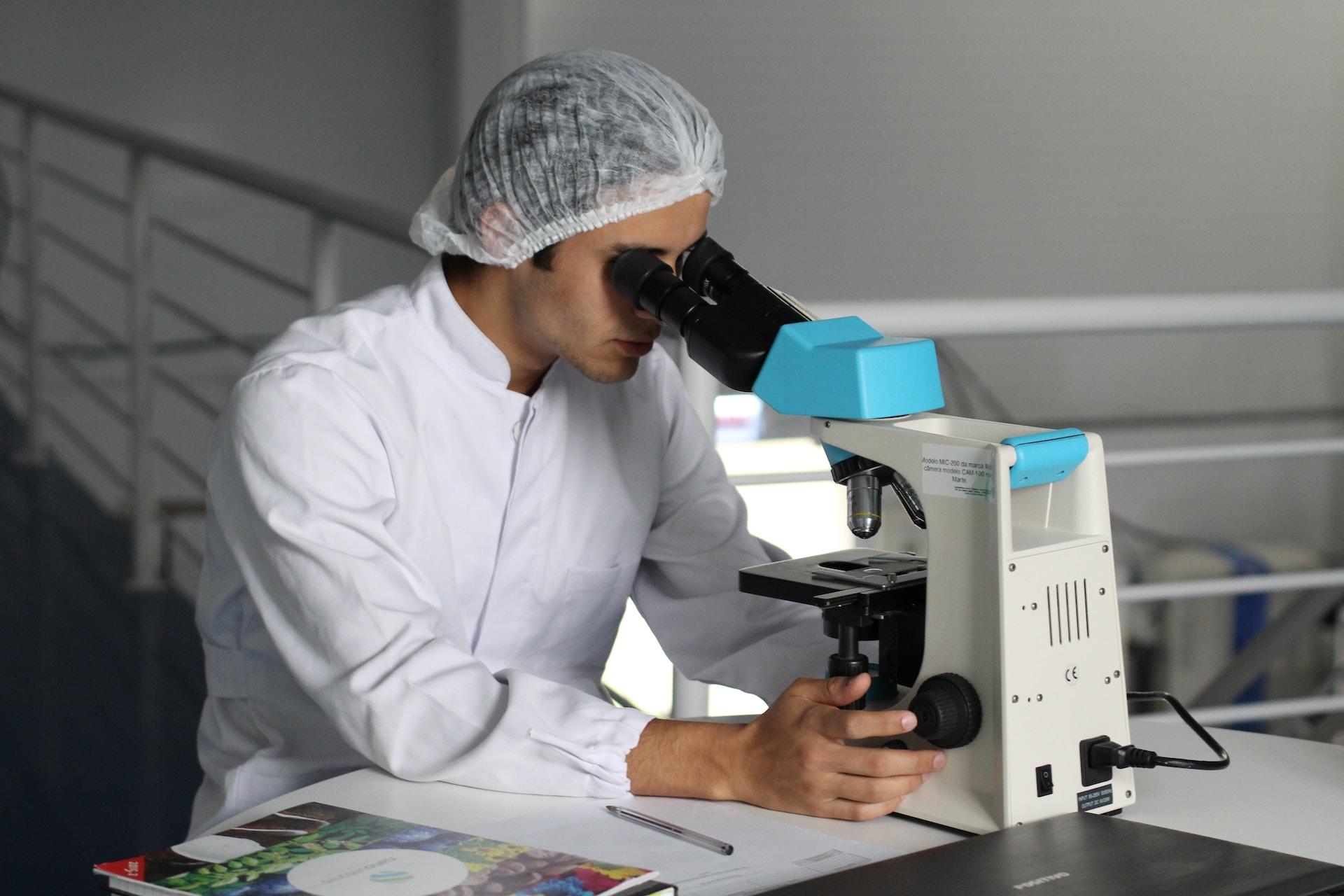 personne en tenue de laboratoire en train de faire des analyses au microscope