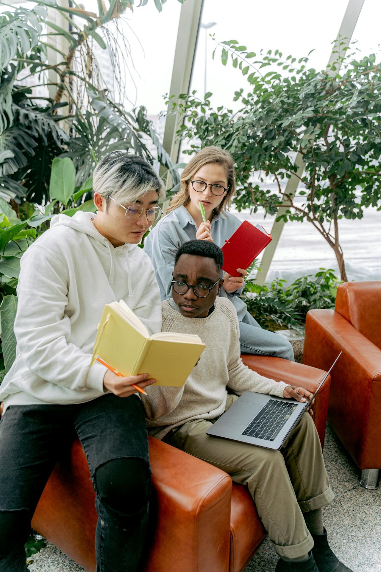 trois etudiants bouquins et ordinateur a la main assis sur un fauteuil orange