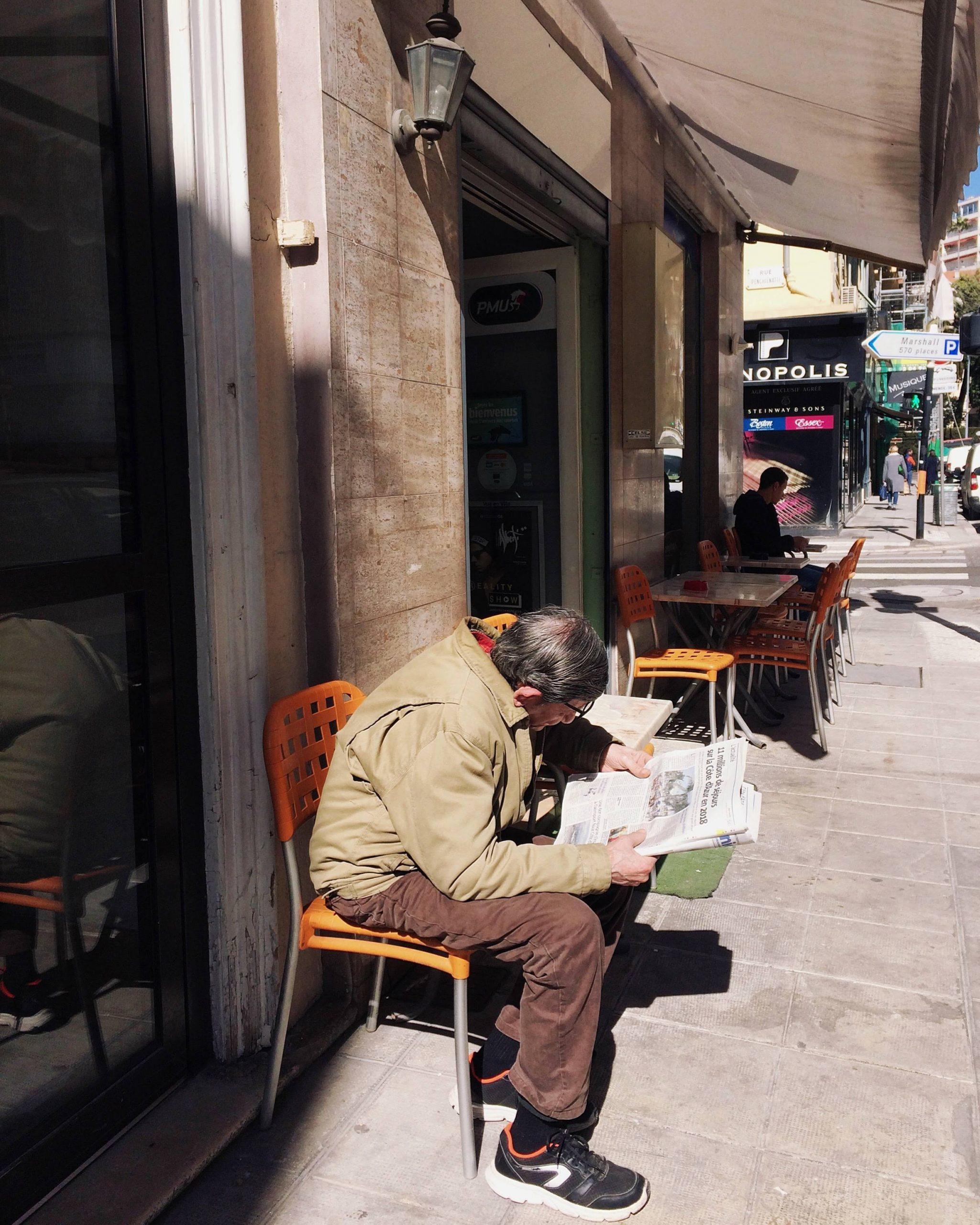 Un homme lit le journal en terrasse.