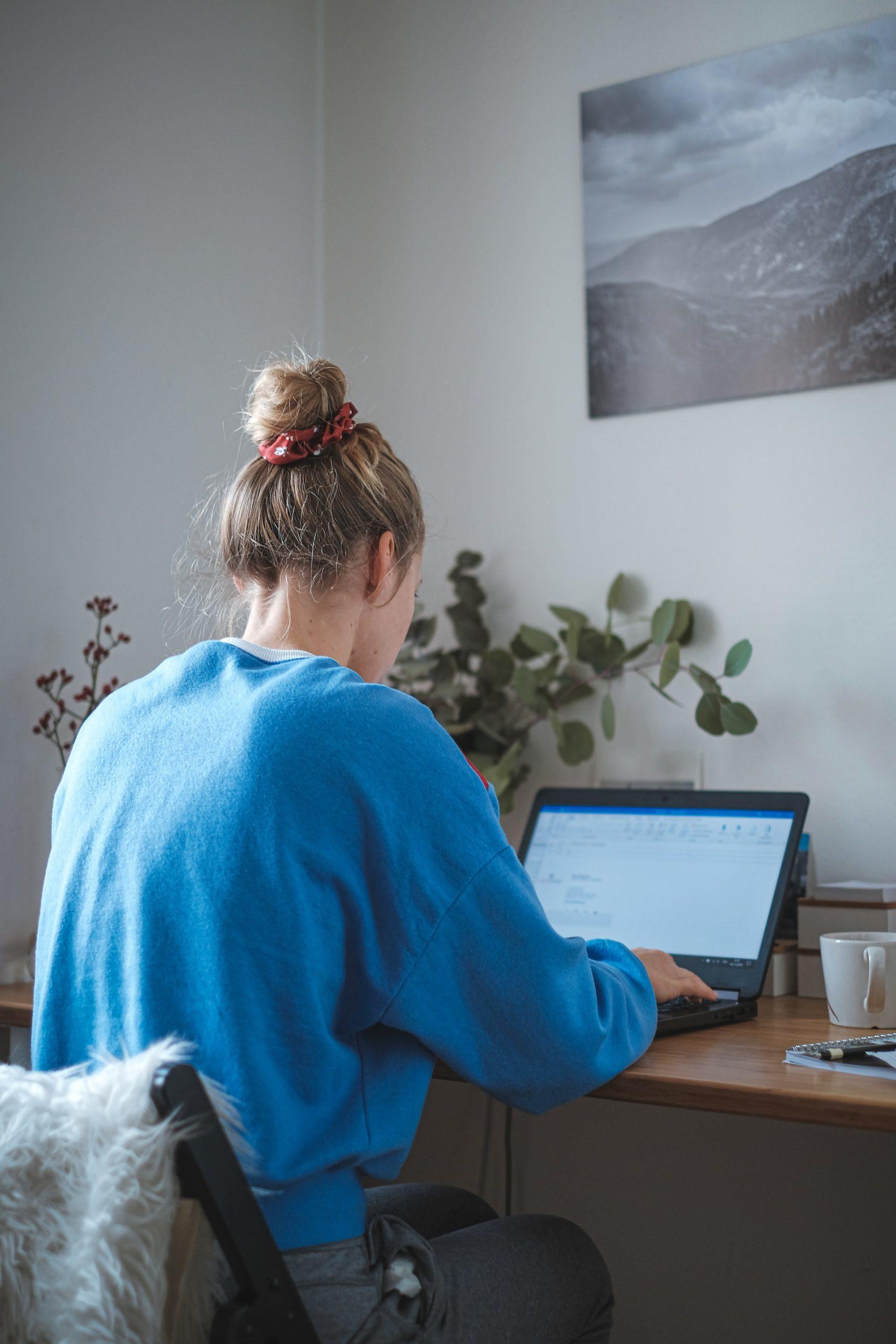 femme en sweat bleu travaillant sur son ordinateur à son bureau 