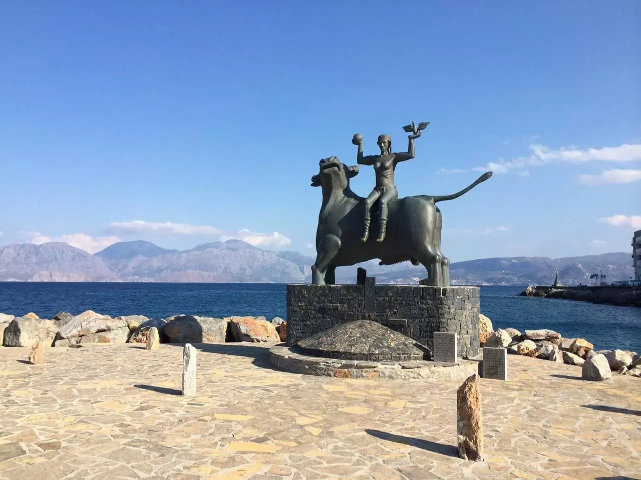 stztue mythologique sur le sable devant la mer et les montagnes