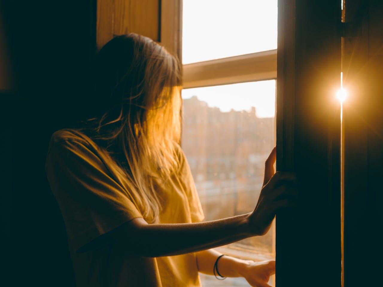 jeune femme a la fenetre devant le soleil triste