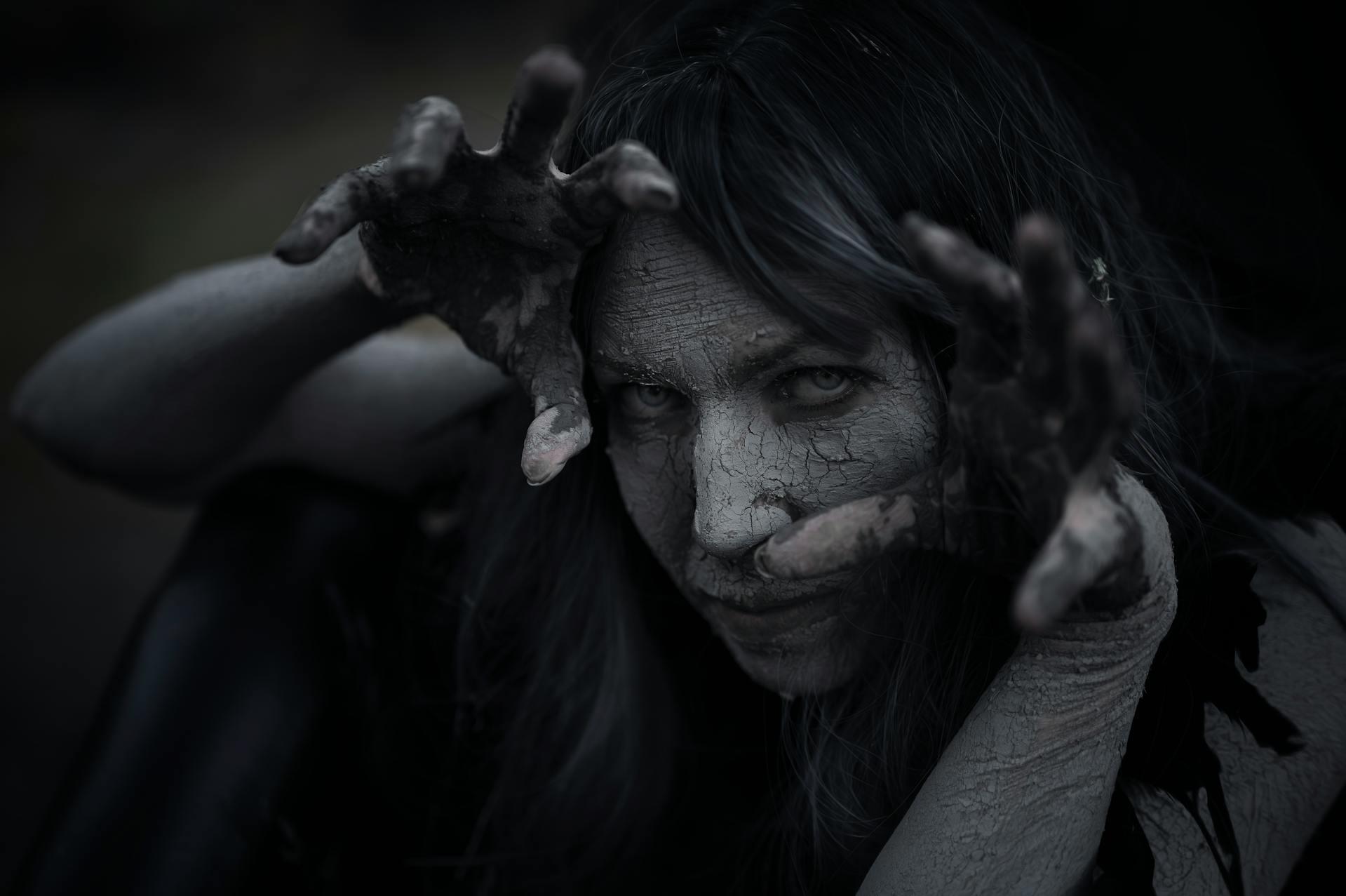 Lady with black hair and face paint making creepy gestures 