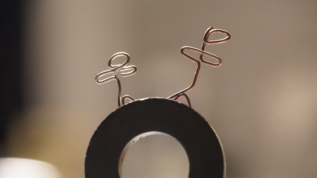 Apstraktna umetnička fotografija koja prikazuje dve figure napravljene od žice postavljene na tamni prstenasti magnet. Minimalistička kompozicija povezuje umetnost, kreativnost i magnetizam.