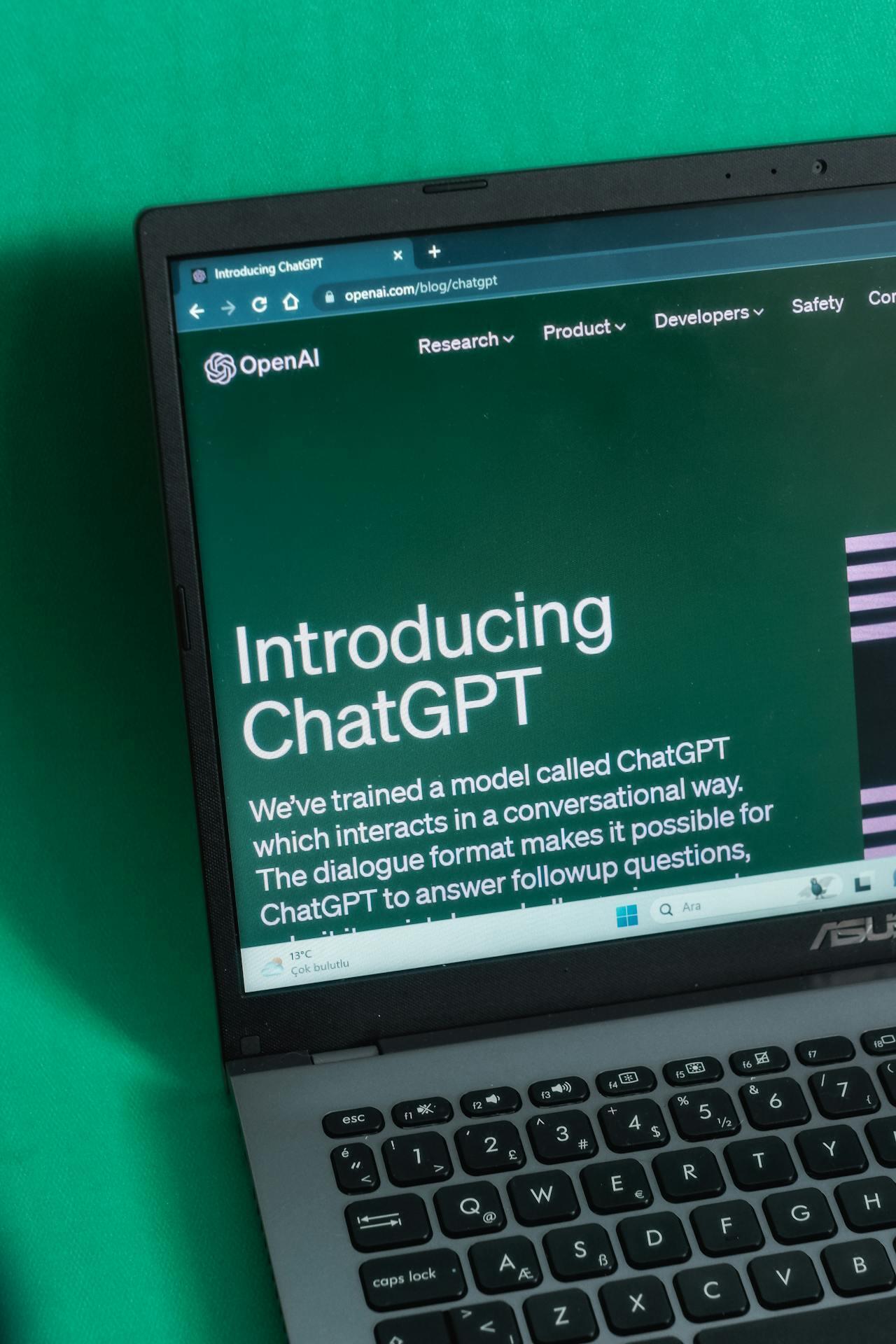 Krupni plan ekrana laptopa na kojem je prikazana veb-stranica „Introducing ChatGPT“ kompanije OpenAI, na pozadini u tirkiznoj boji.