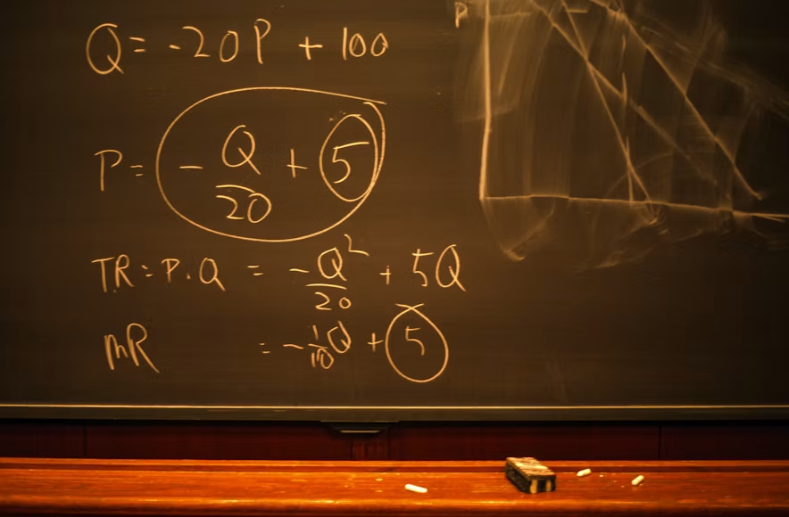 Fotografija prikazuje crnu školsku tablu na kojoj su kredom ispisane matematičke formule, geometrijski oblici. Tabla dočarava autentičnu atmosferu učionice ili naučne laboratorije, naglašavajući duh klasičnog učenja i istraživanja.