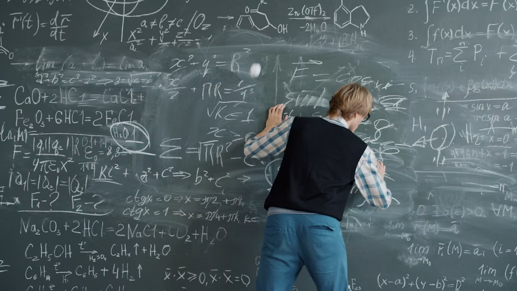 Fotografija prikazuje fokusiranog studenta ili mladog istraživača kako kredom piše složene matematičke jednačine, formule i geometrijske skice na velikoj crnoj tabli. Scena simbolizuje posvećenost učenju, rešavanje kompleksnih problema i nastavak tradicije velikih antičkih mislilaca poput Arhimeda u modernom okruženju.