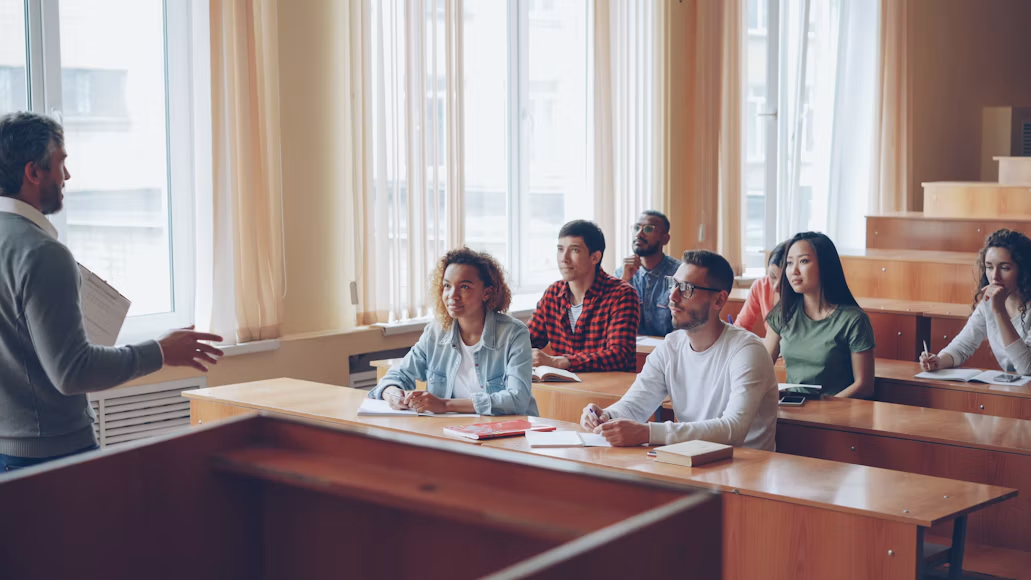 Iskusni profesori u svetloj i modernoj učionici prenose znanje kroz dinamično i zanimljivo predavanje. Nasmejani i motivisani srednjoškolci pažljivo slušaju i učestvuju u razgovoru, što prikazuje opuštenu, ali podsticajnu atmosferu za učenje i pripremu za ispitne izazove.