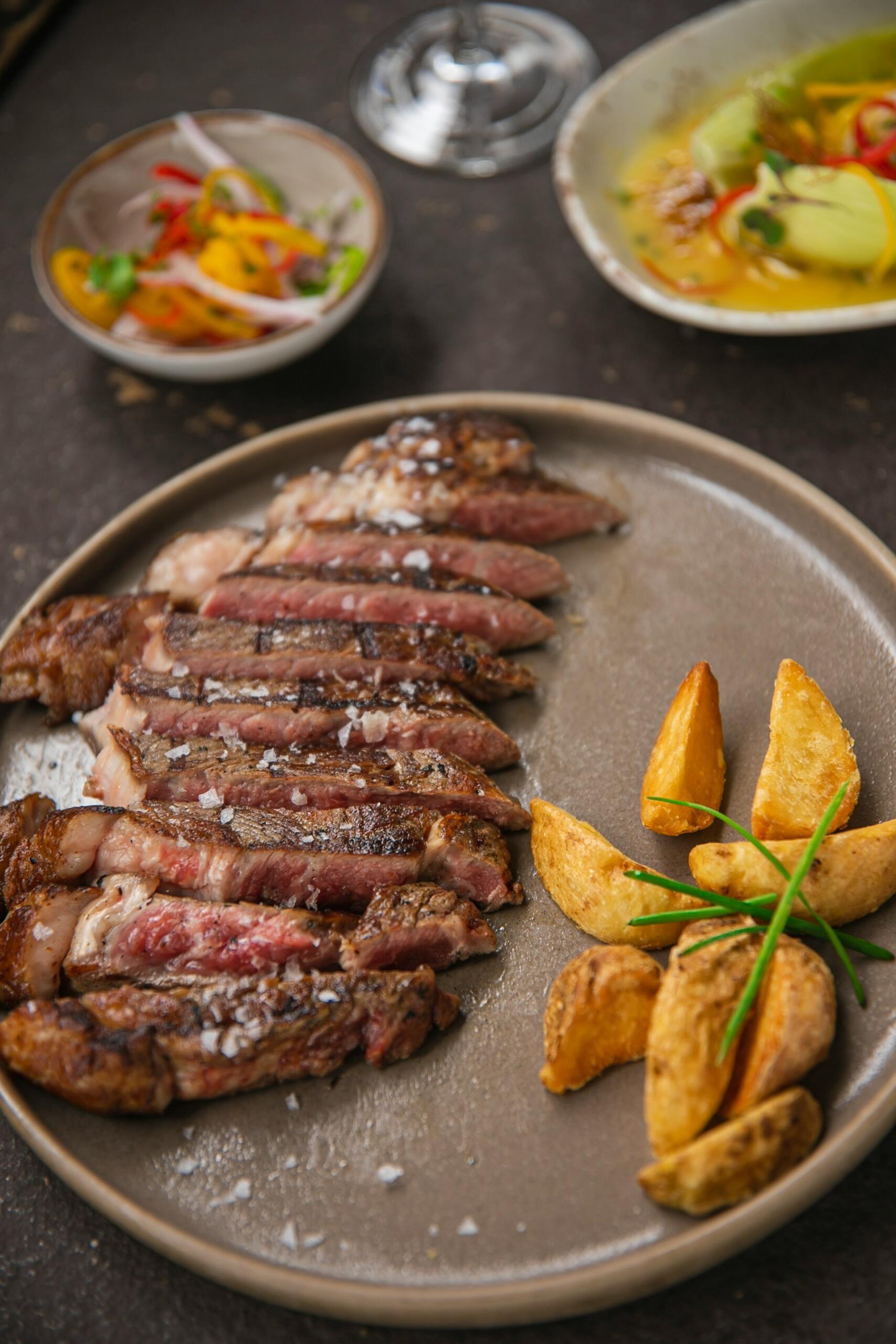  Saftig grillad biffstek med krispiga potatisklyftor och flingsalt, serverad med fräscha tillbehör – en klassisk och smakrik gourmeträtt perfekt för middag eller restaurangupplevelse. Bild av Pablo Merchán Montes via Unsplash+