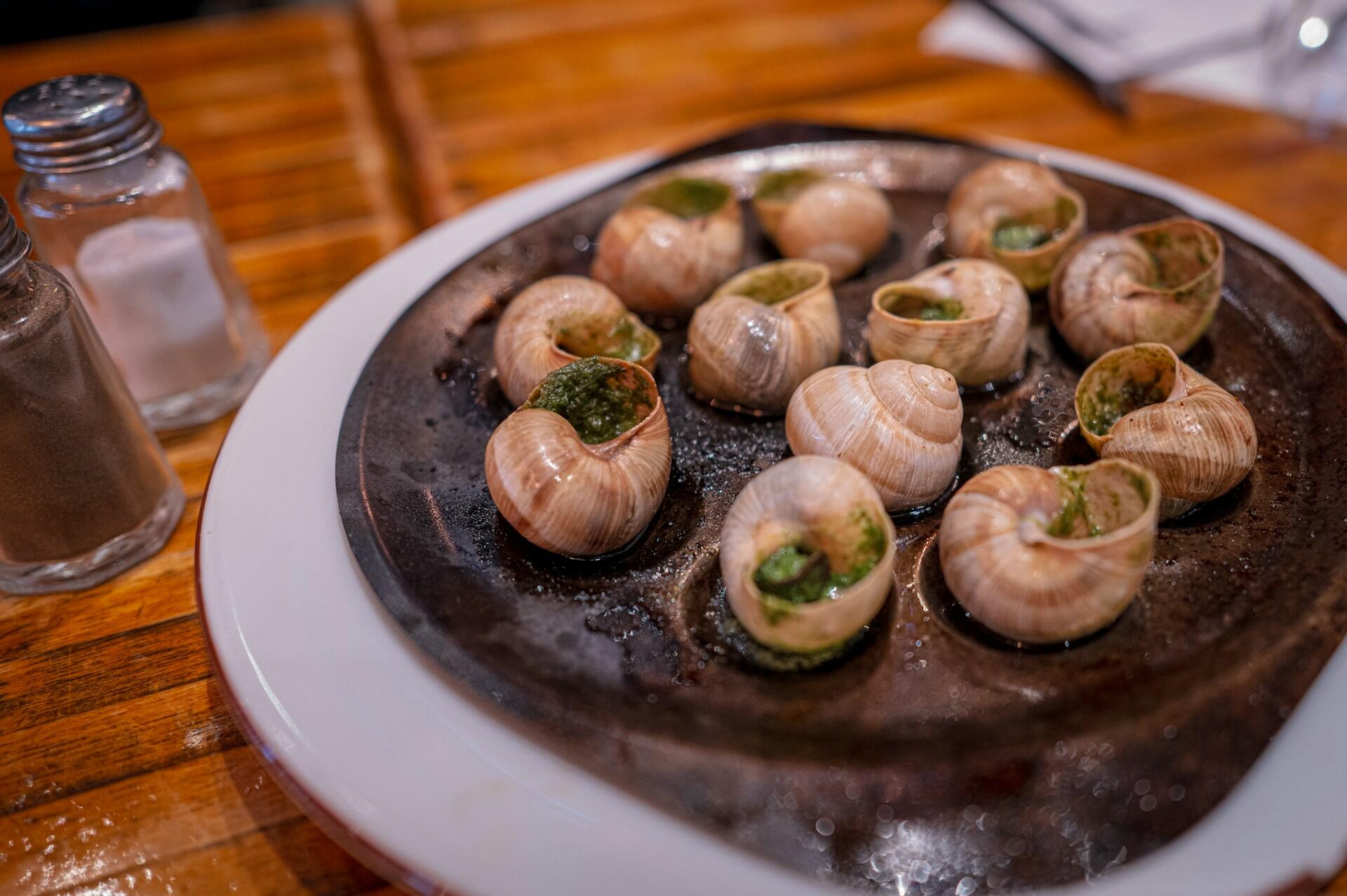 En tallrik med tillagade sniglar "Escargots" står på ett bord.
