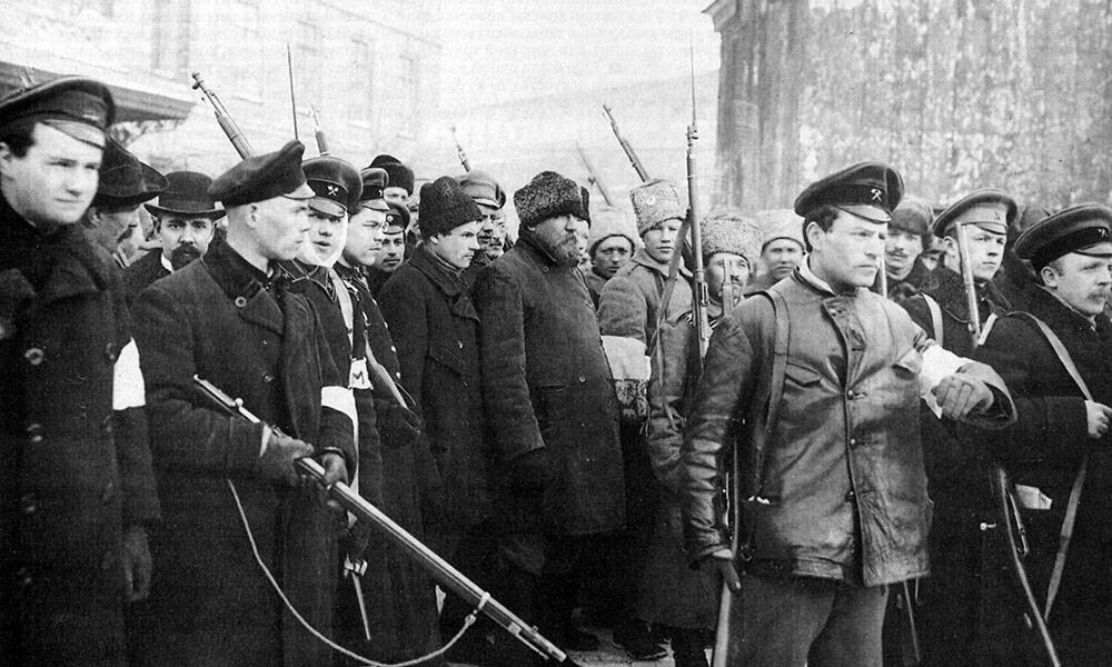 En grupp soldater i historiska uniformer, stående med gevär, i en dyster utomhusmiljö, som påminner om en period av konflikt.