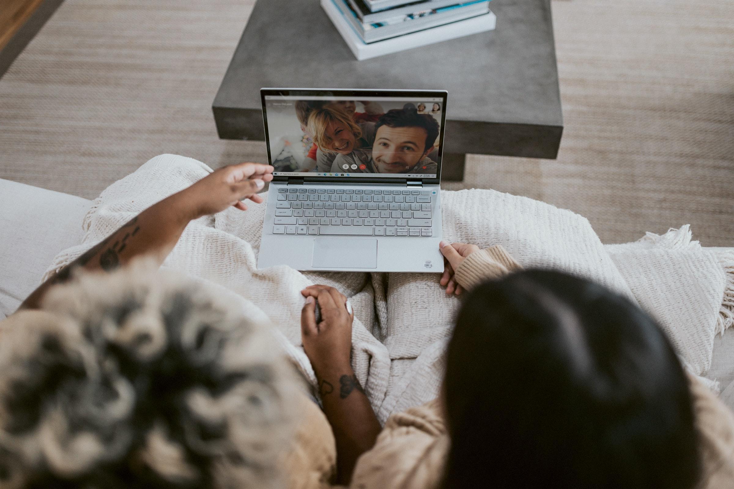 två personer sitter i en soffa och har onlineundervisning via datorn